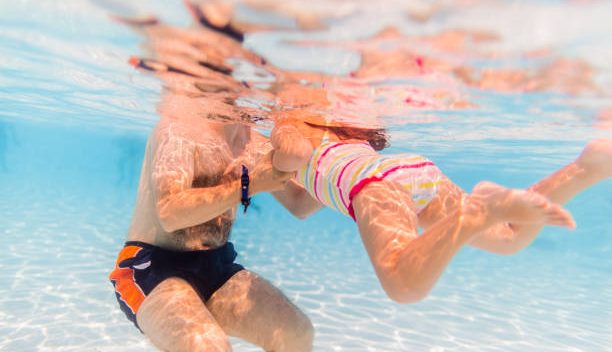 Jeune papa qui apprend à nager à sa fille dans une piscine