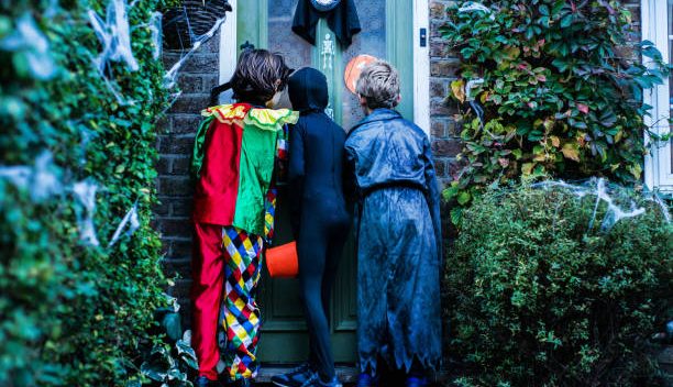 Trois enfants déguisés qui frappent à une porte à Halloween