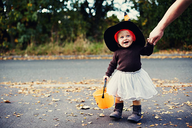 Petite fille déguisée en sorcière qui se promène dans la rue avec un panier orange